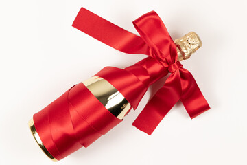 gift bottle of champagne in gold foil wrapped with red silk ribbon bow on white background