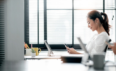 Young asian woman using smartphone while sitting at her office desk in modern office.