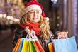 © Светлана Густова - A woman with long hair and a Santa hat near the window of a city store with purchases in colorful, paper bags. New year's shopping