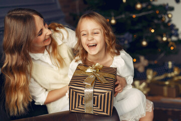 Beautiful mother in a white dress. Family with cristmas gifts. Girls near fireplace.