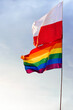 Polska oraz tęczowa flaga z barwami LGBT na tle niebieskiego nieba z białymi chmurami