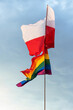 Polska oraz tęczowa flaga z barwami LGBT na tle niebieskiego nieba z białymi chmurami