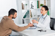 © LIGHTFIELD STUDIOS - Smiling african american doctor giving bottle with pills to patient, while sitting at workplace on blurred background