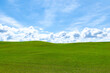 Puffy white clouds and blue sky over a huge beautiful idyllic green grassy field with gently rolling hills in the background
