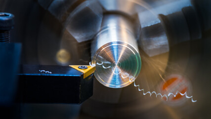 Close-up of turning with sharp tool bit on a dark background. Cutting tool with yellow triangular carbide insert on working lathe. Spiral swarf and motion blur on dural workpiece in chuck. Front view.