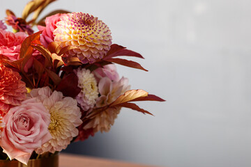 Floral composition of dahlia flowers, roses and autumn leaves. Arty, bright red and pink color  bouquet of flowers on gray concrete background 