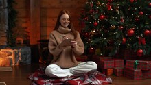 Loving Attractive Young Woman Writing Christmas Greeting Card To Beloved, Closes And Gently Kisses Letter Siting Near Xmas Tree. Cute Redhead Female Writes Wish List For Next New Year To Santa Claus.