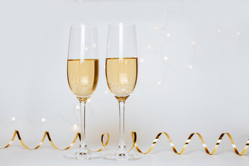 Wall Mural - Two glasses of champagne with lights and ribbons on a white background holiday