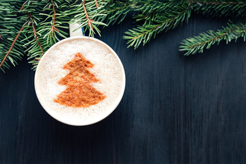 Top view of cup of cappuccino with milk foam topped with cocoa power. Latte art. Dark wooden background and fir tree