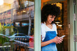 © BONNINSTUDIO/Westend61 - Smiling woman using cell phone in entrance door of a store