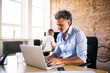 © HalfPoint/Westend61 - Businessman using laptop in office with colleague in background