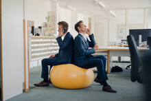 Two Businessman Checking Smartphone With Yellow Fitness  Ball In Foreground