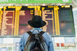 © KIKE ARNAIZ/Westend61 - Young man with hat and backpack looking at arrival departure board at the airport