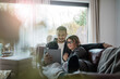 © Robijn Page/Westend61 - Smiling couple lying on couch at home sharing tablet