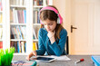 © Larissa Veronesi/Westend61 - Little girl doing homework with headphones and digital tablet