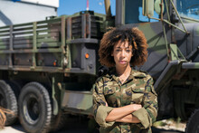 Confident Young Female Military Soldier Standing With Arms Crossed Against Truck At Base On Sunny Day