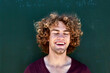 © Martina Ferrari/Westend61 - Portrait of laughing young man with curly hair in front of a green wall