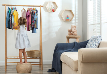 Poster - Little girl choosing clothes on rack in living room