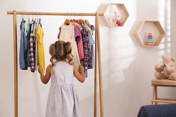 Canvas Print - Little girl choosing clothes on rack in room