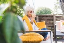 Mature Woman Drinking Juice While Sitting On Sofa In Balcony