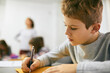© Dangubic/Westend61 - Schoolboy writing on desk in class