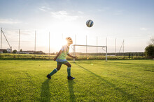 Young Football Player Heading The Ball On Football Ground At Sunset