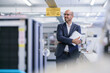 © BELLEVUE/Westend61 - Smiling thoughtful male professional holding digital tablet while looking away at bright factory