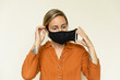 © Nicole Mason/Stocksy - young woman putting on black face mask in studio setting