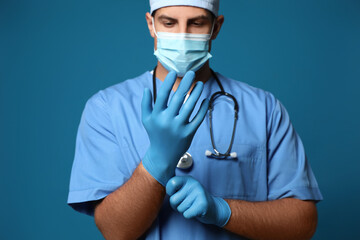 Canvas Print - Doctor in protective mask putting on medical gloves against blue background