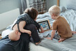 © irina polonina/Stocksy - Young children play in an electronic tablet next to their mother.