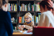 © Sofie Delauw/Stocksy - Elderly woman using smartphone near colleagues in library