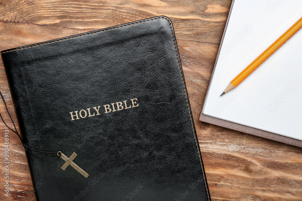 Holy Bible, cross and notebook on wooden table