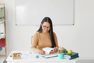 Poster - Asian female teacher sitting at table in classroom