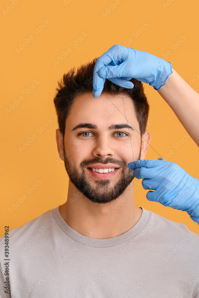 Young man undergoing eyebrow correction procedure on color background
