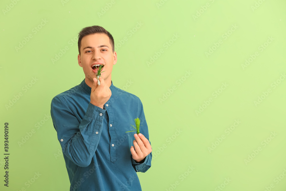 Young man eating wheatgrass on color background