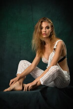Beautiful Slender Blonde Model In White Lace Jumpsuit Posing On Green Fabric Background
