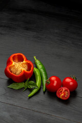 Wall Mural - Cut red sweet pepper and tomatoes and green hot pepper on black background