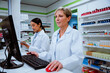 © Prins Productions - Caucasian pharmacist searching for scripts on desktop standing behind counter in pharmacy