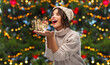 © Syda Productions - winter holidays, magic and people concept - happy smiling young woman in knitted hat and sweater sending magical fairy dust over christmas tree lights on background