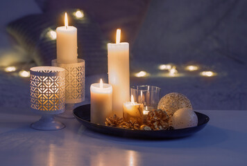 christmas decoration with burning candles on white table against the background of sofa with plaids 