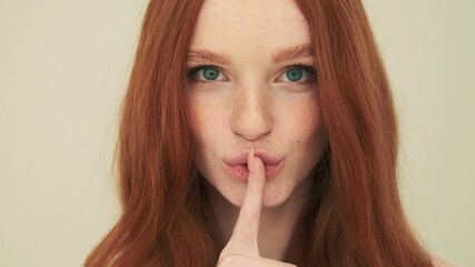 a close-up view of a positive woman is doing secret gesture standing isolated over beige background 
