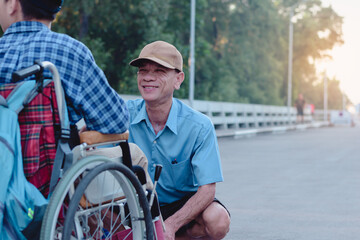 Father looking at asian special child on wheelchair with love on public street,They spend time together in family time, Lifestyle in the education age of disabled children, Happy disabled kid concept.