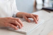 Woman Hands, Fingers Typing On White Wireless Keyboard Lying On Marble Office Table Desk, Side View. Closeup Of Texting A Letter, No Face. Concept Of Work