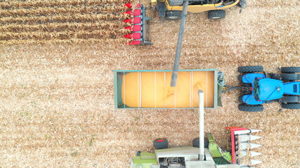 Aerial view of two combines loading off corn grains into tractor trailer. Flying over agricultural machines gathering crop at field. Working process on farm during harvesting. Close up