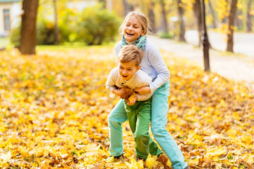 Two children are running on the park in fall leaves. Boy and girl are playing catch up along autumn path in the forest. Happy brother and sister are playing outdoors together. Activities in the fall.