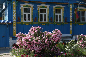 Vintage wooden rural house with ornamental windows, frames in Suzdal town, Russia. Russian traditional national folk style in architecture. Rose garden, summer nature. Suzdal landmark, monument, view