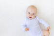 © Any Grant - portrait of a small baby girl 6 months old in a white bodysuit lying on her back on a white bed, space for text