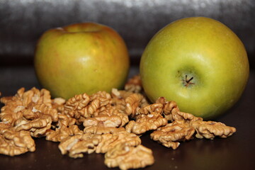 Two large green apples and a scattering of walnuts on a dark background