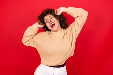 Wall Mural - Young beautiful Arab woman wearing beige sweater against red background relaxing and stretching, arms and hands behind head and neck smiling happy