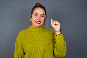 Young beautiful hispanic woman wearing green sweater against gray background pointing up with fingers number ten in Chinese sign language Shi